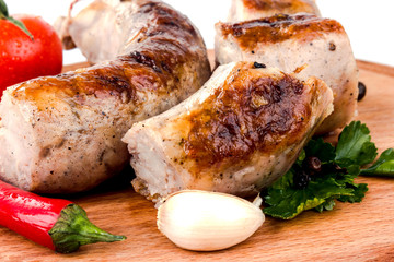 fried pork sausages on a barbecue on a wooden plate with cherry tomatoes and hot peppers