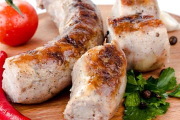 fried pork sausages on a barbecue on a wooden plate with cherry tomatoes and hot peppers