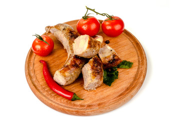 fried pork sausages on a barbecue on a wooden plate with cherry tomatoes and hot peppers