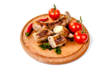 fried pork sausages on a barbecue on a wooden plate with cherry tomatoes and hot peppers