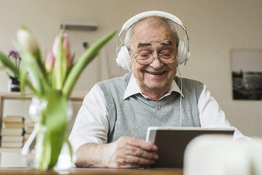 Senior man using mini tablet and headphones for skyping at home