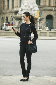 Spain, Catalunya, Barcelona, young black dressed businesswoman looking at her smartphone in front of a street