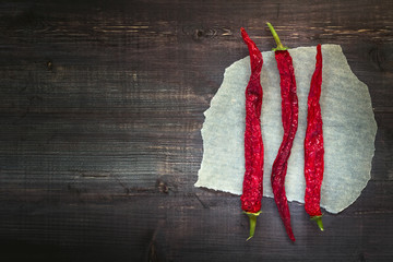 Three chili peppers on a piece of paper. Wooden simple background, blank space