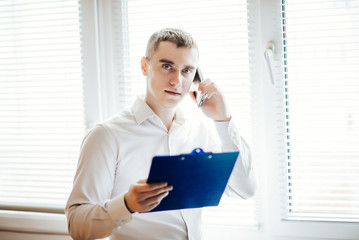 businessman with the tablet stands near a window and talking on the phone