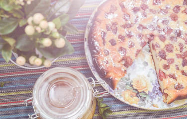cherry pie on the colorful tablecloth with green twig and honey