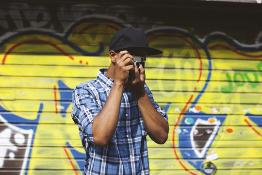 Young man with baseball cap and camera taking photos in front of roller shutter