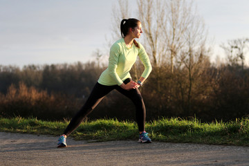 Young female runner doing exercise in evening sun