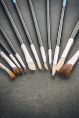 Vintage stylized row of old paintbrushes on rough stone background, shallow depth of field.