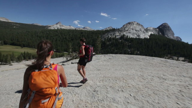 Hikers people hiking in Yosemite. Hiker couple walking on hike wearing backpacks. Happy sporty couple walking down from the Pothole Dome, Yosemite National Park, California, USA.