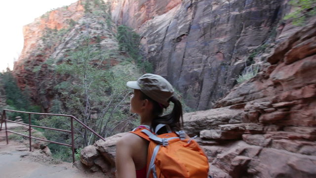 Hiker woman hiking in Zion National Park. Happy female hiker trekking on walking path in Zion Canyon wearing backpack. Healthy lifestyle image with multiracial Asian Caucasian girl in Utah, USA.
