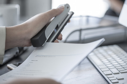 Close-up of woman at desk stapling a document
