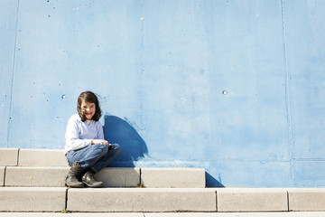Portrait of smiling little girl sitting on steps in front of blue wall