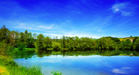  Lake and green trees on sky background.
