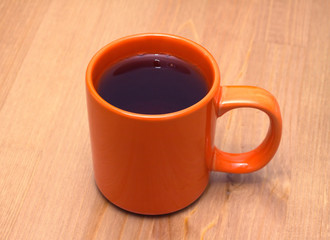 Orange cup from ceramics with tea on brown wooden table closeup