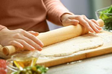 Woman rolling out a pizza dough on a wooden board, close up