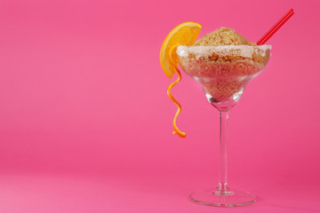 Margarita glass with brown sugar, cocktail straw and orange slice on pink background