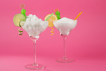 Margarita glasses with lump, granulated sugar, cocktail straws and citrus slice on pink background