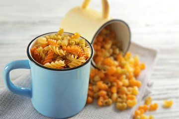 Raw pasta in mugs on wooden table closeup