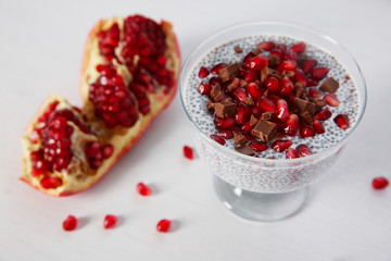 Chia seeds pudding with pomegranate grains and chocolate chips in glass saucer on white background
