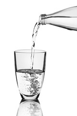 Pouring water from bottle into glass over grey background