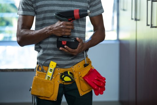 Mid section of manual worker holding a drill machine