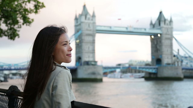 People in London - woman happy by Tower Bridge. Multicultural young professional smiling and laughing enjoying view of River Thames. Beautiful young female tourist on travel in England, Great Britain.