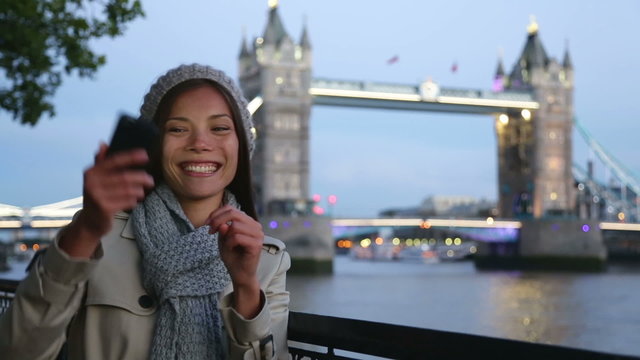 Asian tourist in London taking self-portrait photo smiling happy showing victory v hand sign with Tower Bridge in background. Travel and tourism concept with beautiful girl traveling in London England