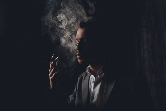 Attractive young man with cigar and smoke on black background