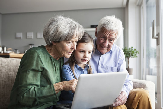 Grandparents and their granddaughter sitting together on the couch looking at digital tablet