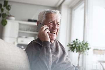 Portrait of laughing senior man telephoning with smartphone at home