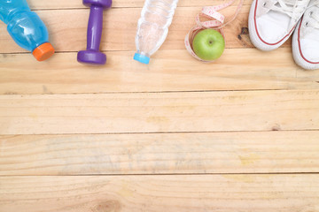 An apple, a measuring tape and dunbbell on wood