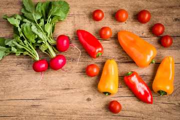 Sweet peppers, cherry tomatoes and radishes on a wooden background