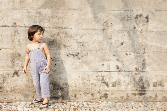 Little boy standing in front of concrete wall in summer