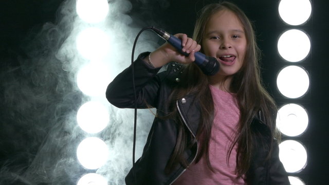 Young Asian American girl singing and bowing with smoke and stagelight in background.