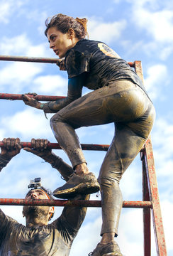 Participants in extreme obstacle race climbing over hurdle