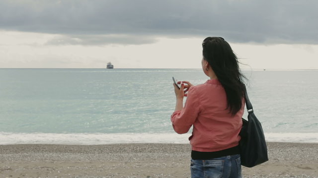 Woman doing landscape photography. Woman with smart phone makes the photo of the landscape on a cloudy day, standing on the Mediterranean seafront. 