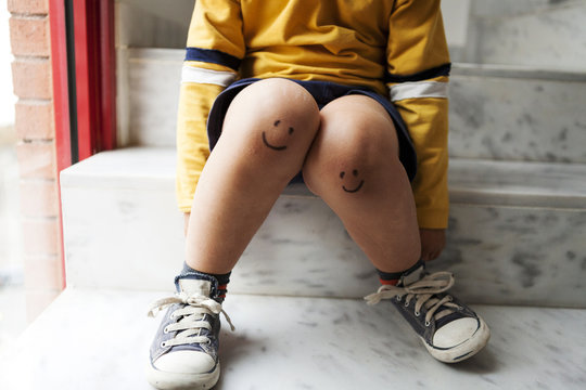 Boy sitting on stairs with smiley faces on his knees