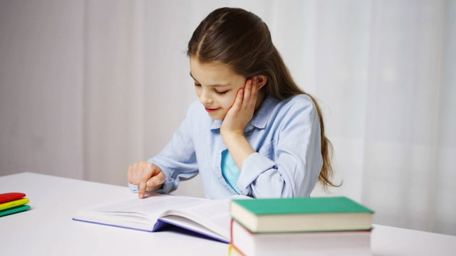 happy school girl reading book or textbook at home