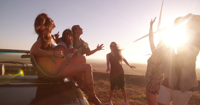 Hipster friends enjoying road trip with a guitar during sunset