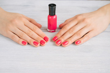 Female hands with red manicure and nail polish bottle on a woode