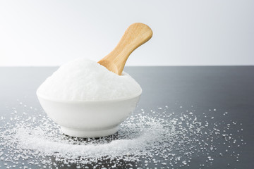 White granulated sugar in white cup on dark wooden background.