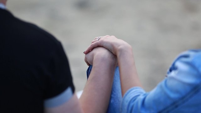 Couple sitting on beach near sea, hands on knees