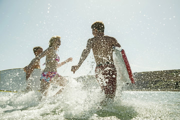 Three teenagers with surfboards running at waterside of the sea