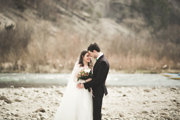 Fototapeta na wymiar Beautifull wedding couple kissing and embracing near river with stones