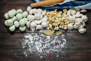 Different types of meat dumplings - russian pelmeni on wooden background
