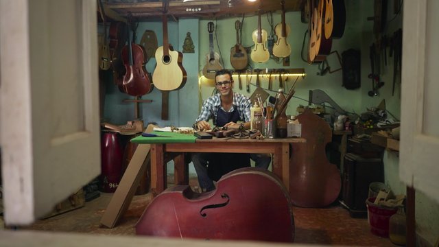 Lute maker shop and acoustic music instruments: portrait of an artisan sitting at his desk and smiling at camera. 
