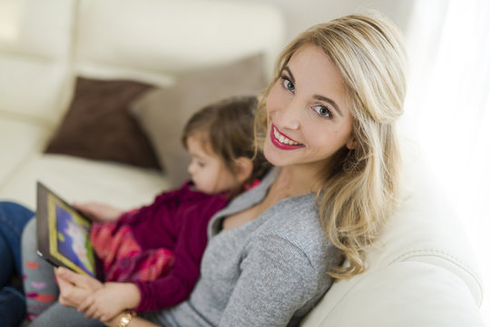 Portrait of smiling woman sitting with her little daughter on couch in the living room