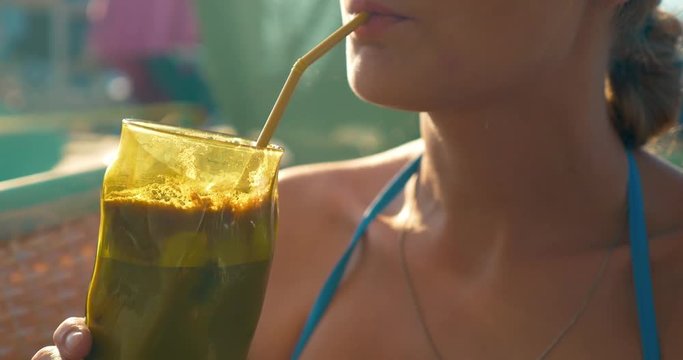 Closeup shot of a glass with ice coffee in hands of young woman. She is drinking it through the straw.
