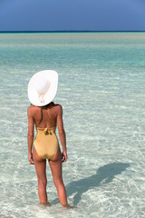 Fototapeta na wymiar femme avec un chapeau blanc dans l'eau de mer transparente