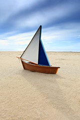 small wooden ship toy model in the sand on the beach